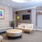 An upscale seating area with a white sofa, a round gold ottoman, and colorful abstract artwork