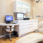 A high-tech dental operatory with a white patient chair, dual computer monitors, and sleek cabinetry