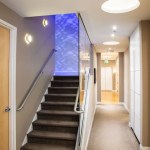A modern office hallway featuring a dark wood staircase with a vibrant blue backlit wall panel