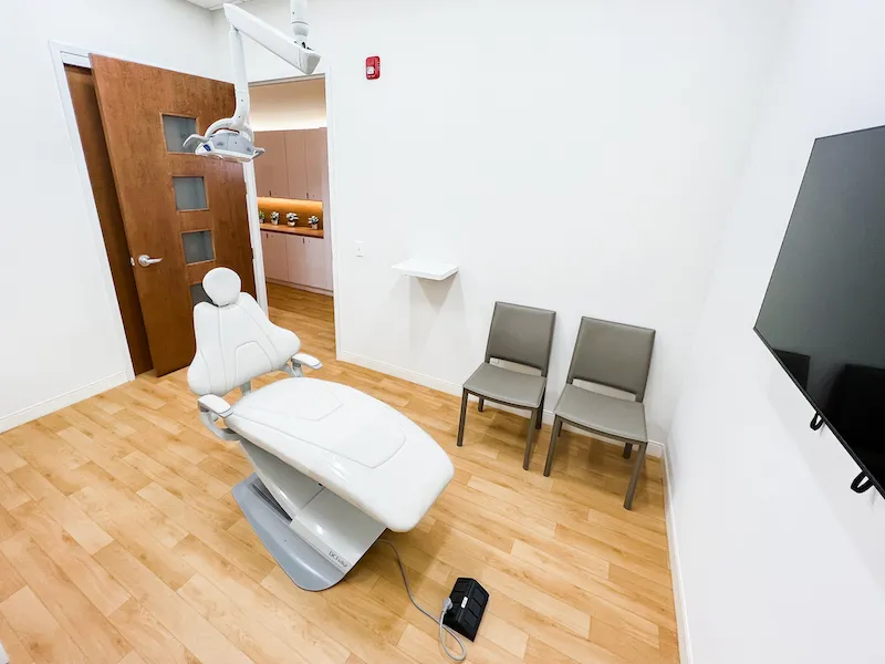 A clinical operatory room featuring a modern patient chair, hardwood floors, and a wall-mounted monitor