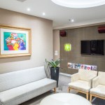 A patient waiting lounge with white leather seating, a wall-mounted TV, and framed colorful art