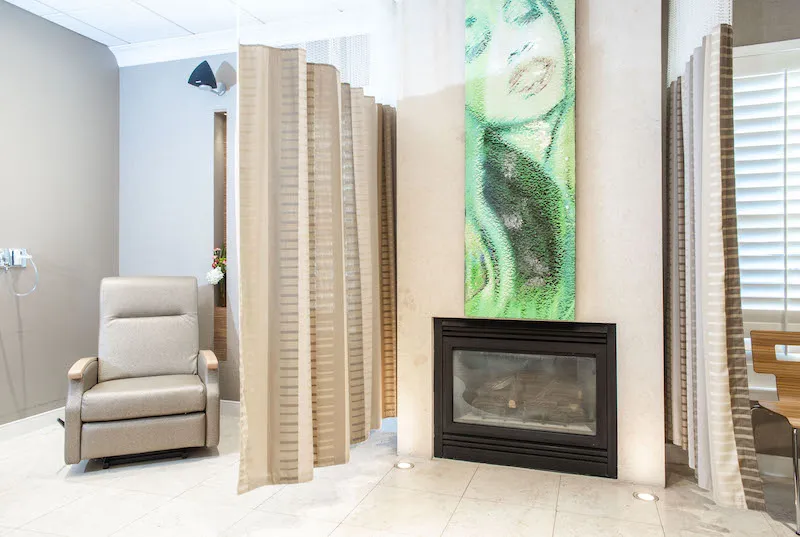 A patient recovery area with a comfortable recliner, a contemporary fireplace, and a large green abstract painting.