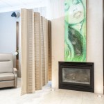 A patient recovery area with a comfortable recliner, a contemporary fireplace, and a large green abstract painting.