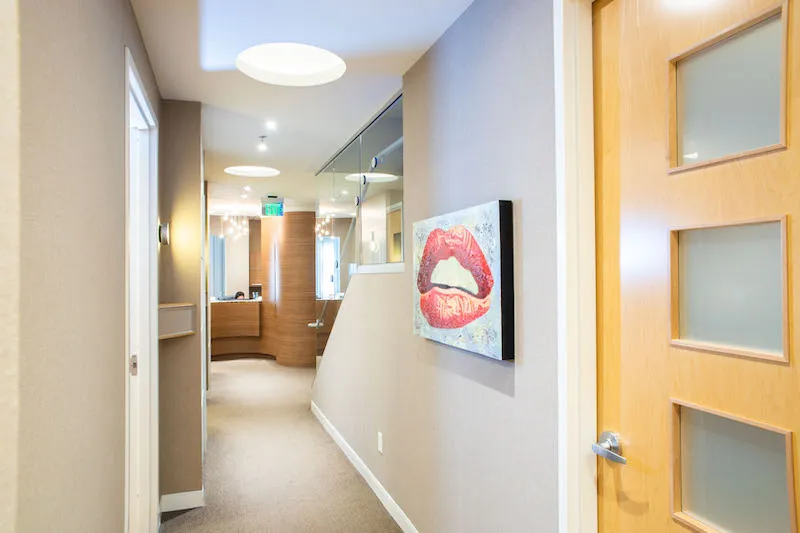 A clean hallway with light wood doors and a wall-mounted digital screen showing a patient's smile