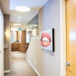 A clean hallway with light wood doors and a wall-mounted digital screen showing a patient's smile