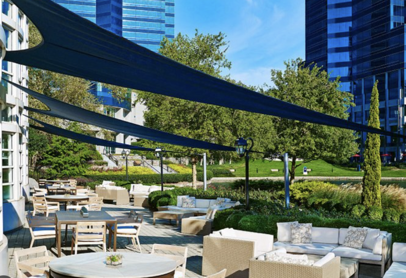 An outdoor patio area with modern white furniture and blue shade sails, likely a relaxation area for patients or staff