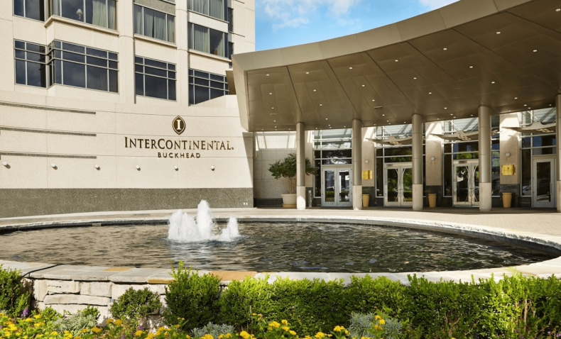 The exterior entrance of a modern office building featuring a circular fountain and manicured landscaping.