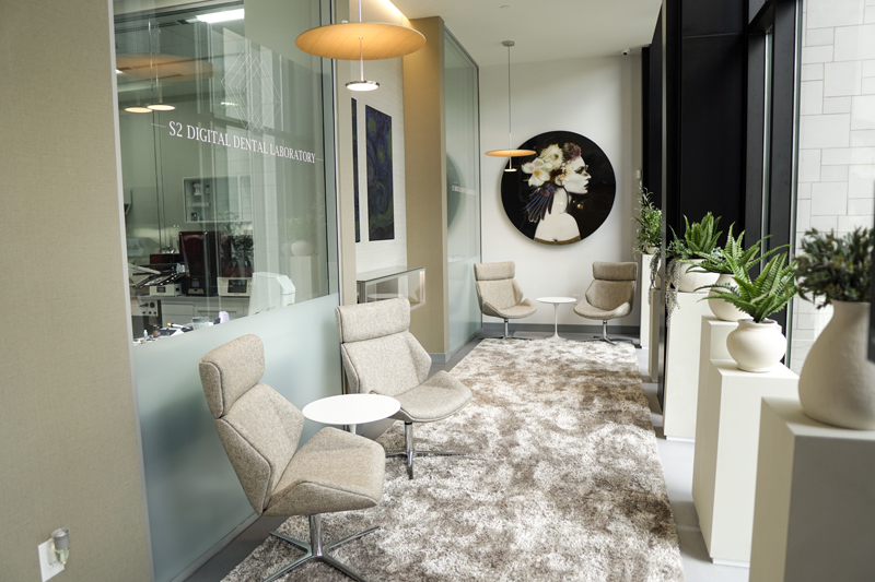 A bright lobby area with large windows, several white seating pods, and a patterned area rug over a light-colored floor