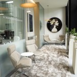 A bright lobby area with large windows, several white seating pods, and a patterned area rug over a light-colored floor