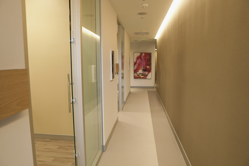 A minimalist hallway with smooth tan walls, a glass door, and recessed warm lighting