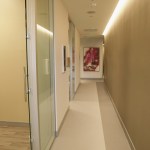 A minimalist hallway with smooth tan walls, a glass door, and recessed warm lighting