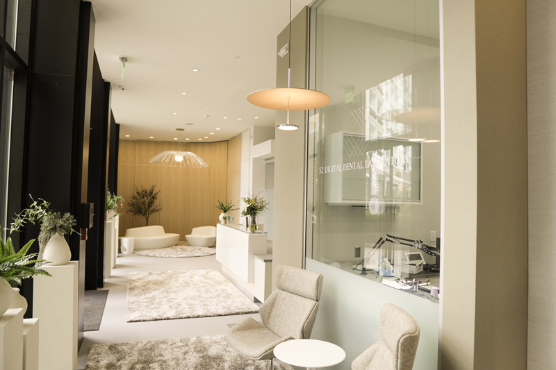 A wide view of an open-concept waiting area with modern white sofas, glass partitions, and indoor greenery
