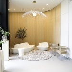A patient lounge area with neutral-toned walls, decorative plants in white tall planters, and plenty of natural light from floor-to-ceiling windows