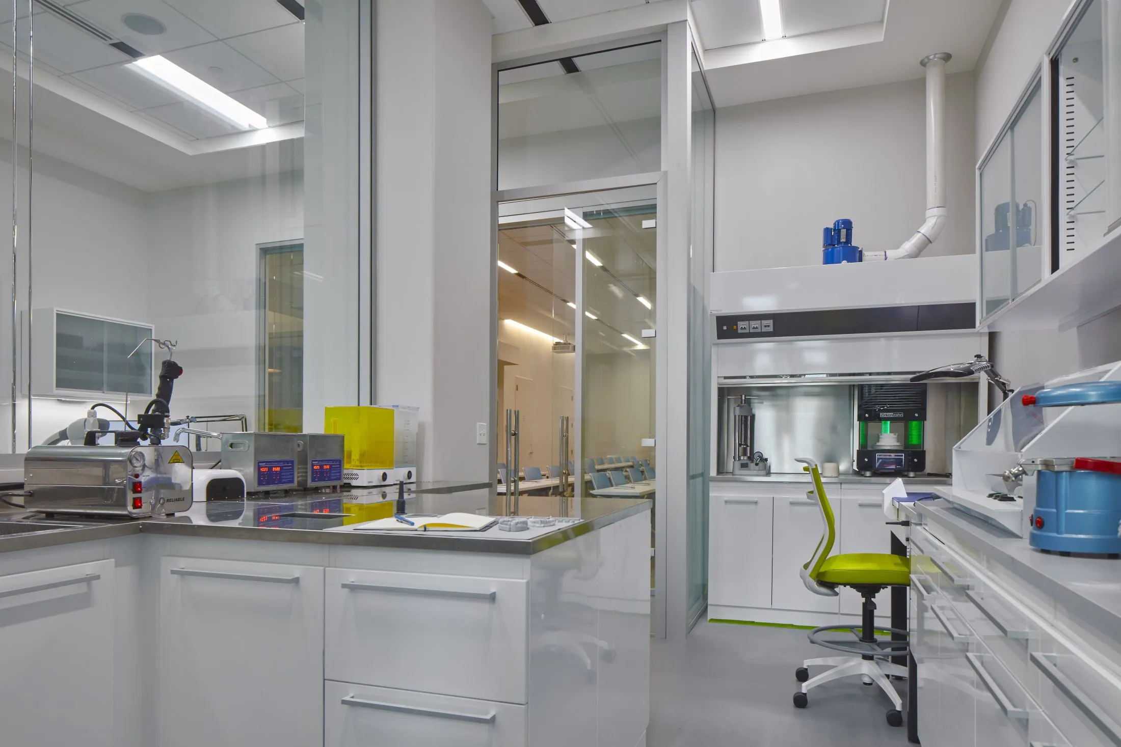 A brightly lit, modern medical laboratory featuring white counters, stainless steel equipment, and a sterile workspace
